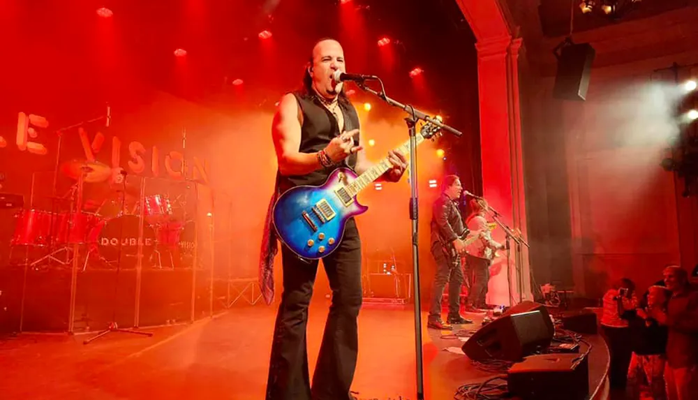 A band is performing energetically on stage with vibrant red lighting and an engaged audience