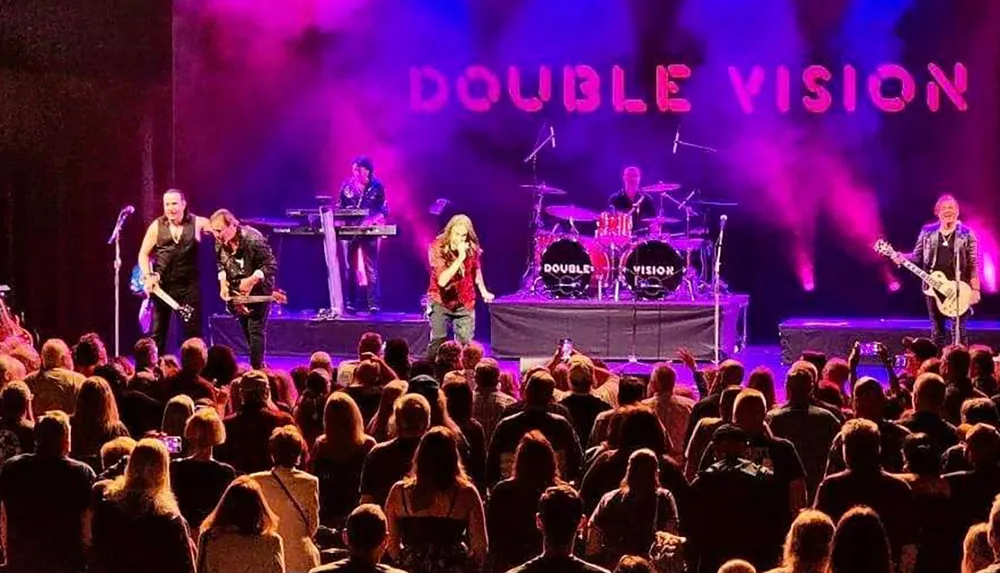 A rock band named Double Vision is performing on stage in front of a large audience