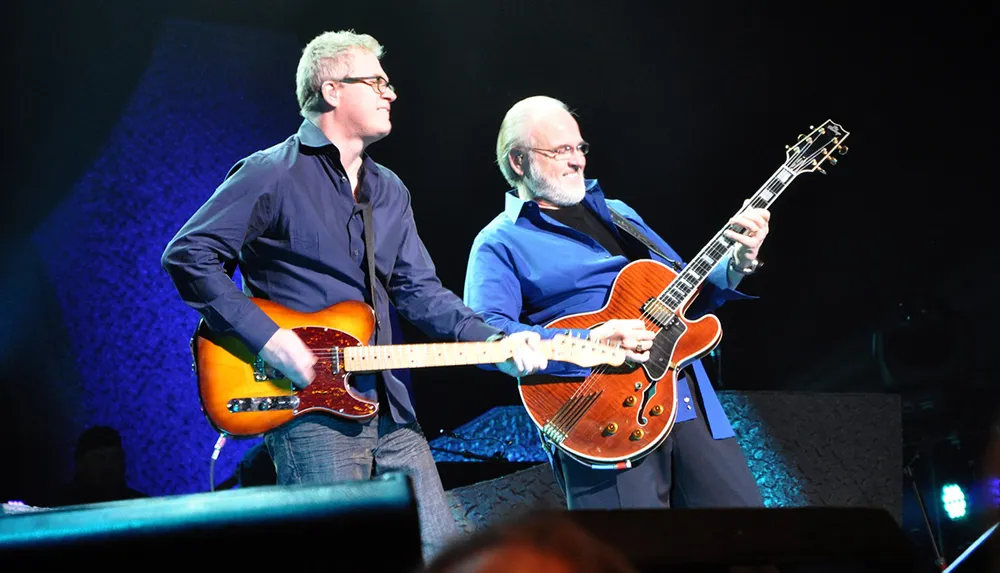 Two musicians are energetically playing electric guitars on stage