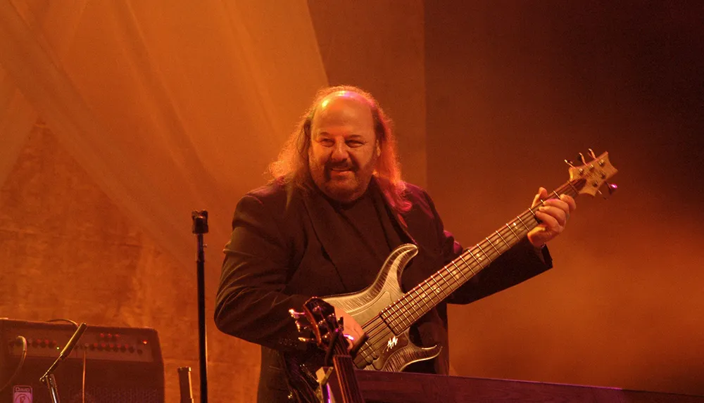 A musician is playing a bass guitar on stage under warm lighting