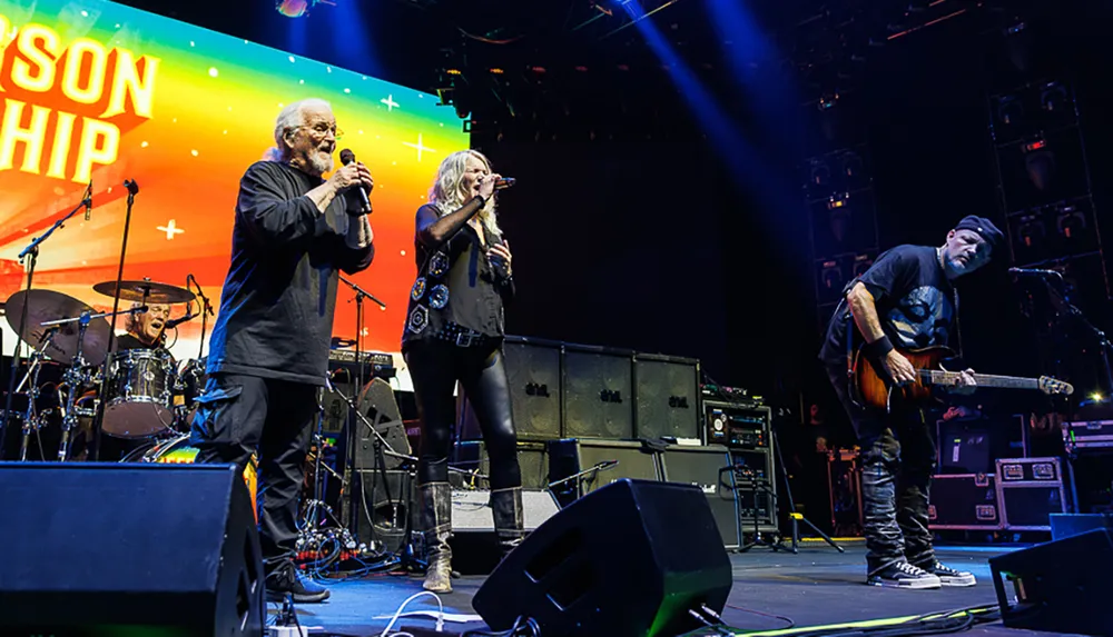 A band performs energetically on stage with a colorful backdrop and musicians playing various instruments