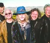 A group of five people dressed stylishly in jackets and hats pose together outdoors with a scenic landscape in the background