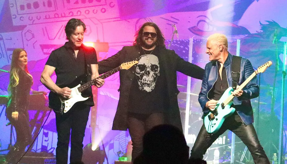 Three musicians with two playing electric guitars are performing energetically on stage under colorful lighting