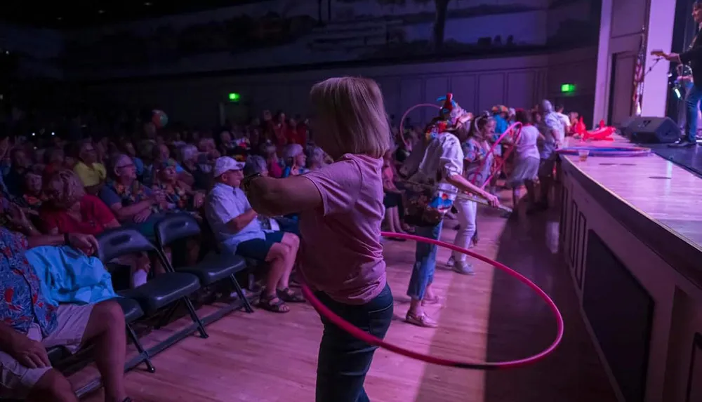 A group of people are enthusiastically hula hooping near a stage in front of an audience