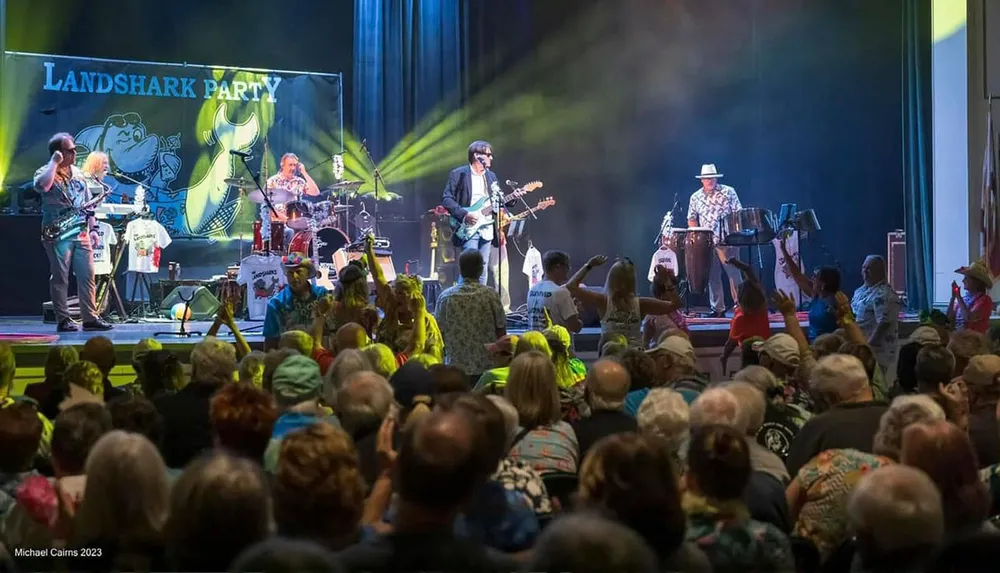 A band is performing on stage at a lively concert with a crowd of people enjoying the music in front of a colorful backdrop