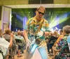 A saxophonist in a tropical shirt plays energetically among an audience at a lively indoor concert