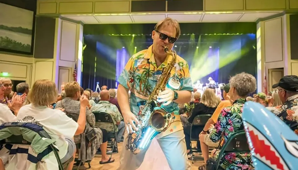 A saxophonist in a tropical shirt plays energetically among an audience at a lively indoor concert