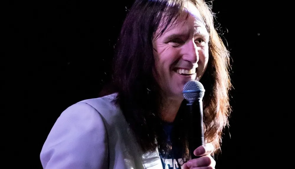 A person with long hair is smiling while holding a microphone on stage