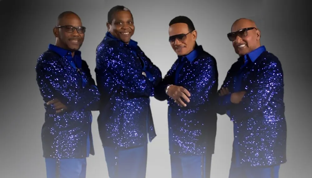 Four men are wearing matching blue sequined jackets and posing confidently against a neutral background