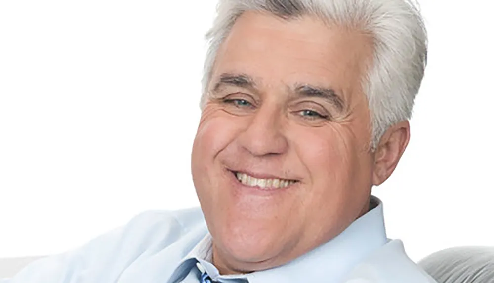 A smiling man with gray hair wearing a light blue shirt