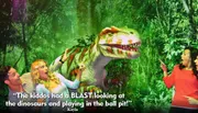 Three people appear to be playfully interacting with a Tyrannosaurus rex in a staged jungle setting.