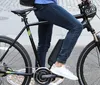 A person wearing blue jeans and white sneakers is riding a black electric bicycle on a city street