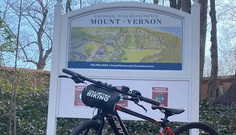 A bicycle is parked in front of a sign for George Washingtons Mount Vernon with a map and admission information