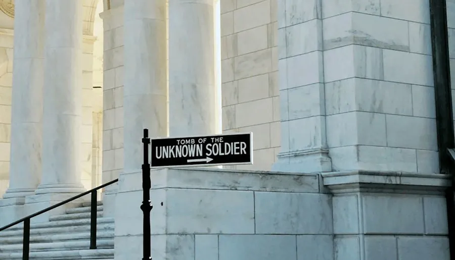 A sign indicating the direction to the Tomb of the Unknown Soldier is displayed in front of a marble building with columns.