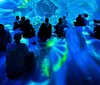 Two people stand and sit on platforms amidst a vibrant immersive digital art installation with colorful abstract jellyfish-like forms