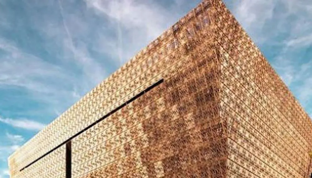 The image shows a close-up view of a modern building with a perforated bronze-colored facade against a blue sky