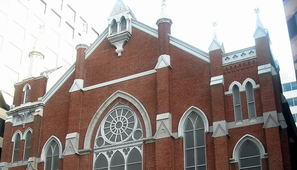 The image shows a red brick Gothic Revival church facade with pointed arches and decorative stone details