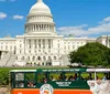 A hop-on hop-off tour trolley passes in front of the US Capitol building on a sunny day