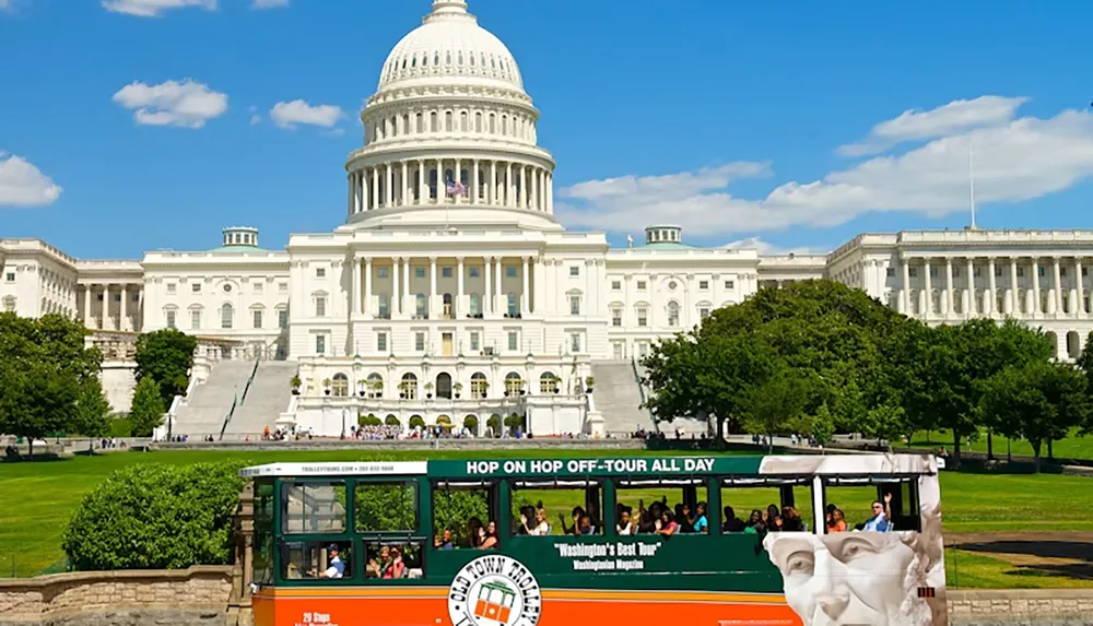 A hop-on hop-off tour trolley passes in front of the US Capitol building on a sunny day