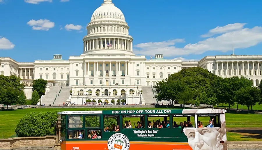 A hop-on hop-off tour trolley passes in front of the U.S. Capitol building on a sunny day.