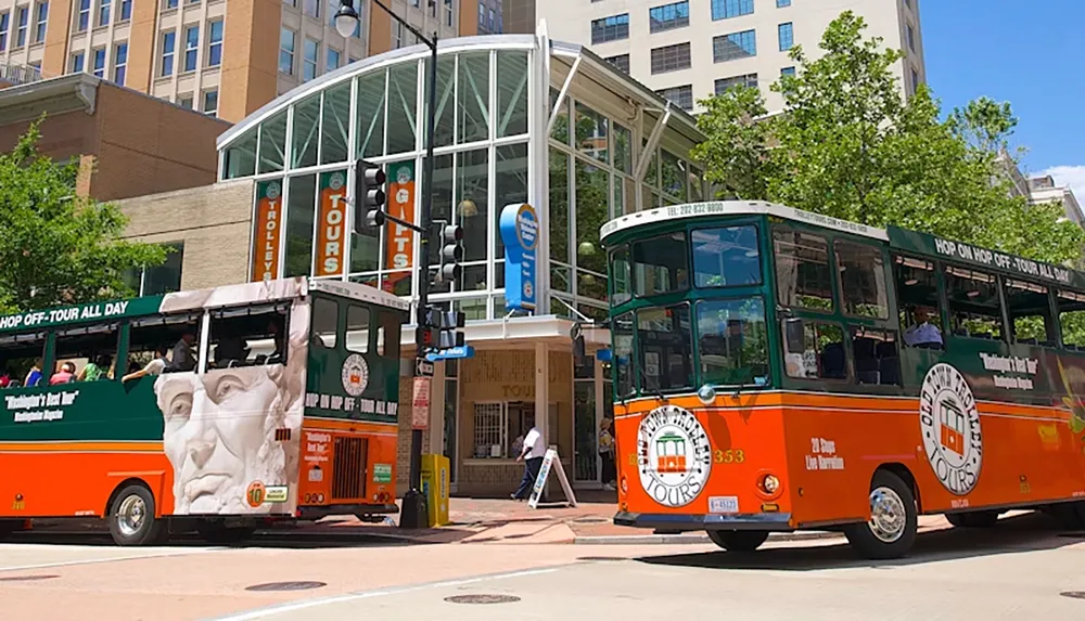 Two open-air tour buses marked with Hop On Hop Off and Old Town Trolley Tours are parked in front of a tours and gifts building in a city setting