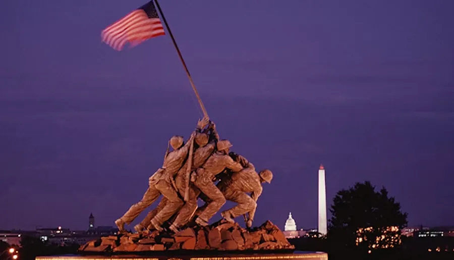 The image depicts the Iwo Jima Memorial with the Washington Monument and Capitol Building illuminated in the background at dusk.