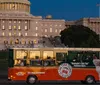 A trolley tour bus with passengers is parked at night near a brightly lit Capitol building