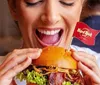 A person is excitedly holding a burger with a Hard Rock Caf flag about to take a bite