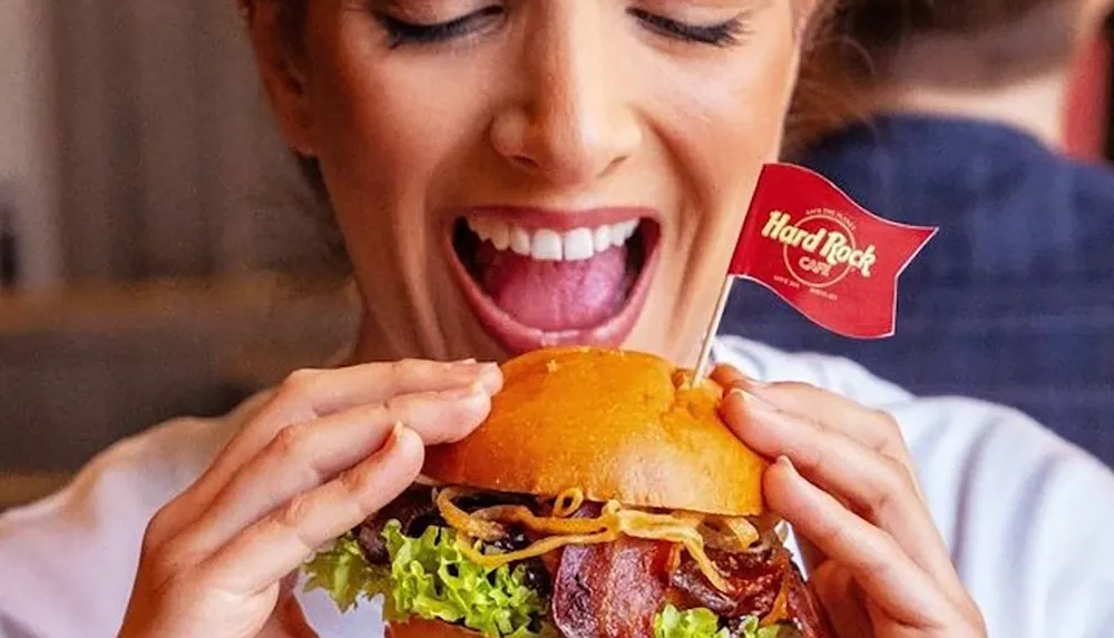 A person is excitedly holding a burger with a Hard Rock Caf flag about to take a bite