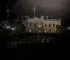 The image shows the White House at night illuminated with dim lights against a dark sky