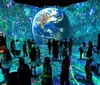 The image shows people in an immersive digital art exhibit featuring vibrant colors and a large projection of Earth on the wall