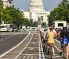 A group of five people wearing helmets pose with bikes in front of the US Capitol building on a sunny day