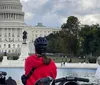 A group of five people wearing helmets pose with bikes in front of the US Capitol building on a sunny day