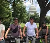 A group of five people wearing helmets pose with bikes in front of the US Capitol building on a sunny day