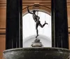 The image depicts a bronze statue of Mercury atop a pedestal within an interior space with tall columns and a skylight