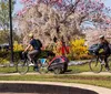 Three people with bicycles pose in front of the Smithsonian Institution Building surrounded by greenery and flowers