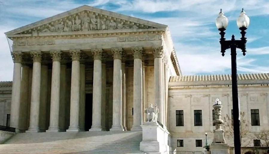 The image shows the front view of a neoclassical building with tall columns and a detailed pediment, likely a government or judicial structure under a blue sky.