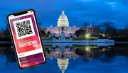 A smartphone displaying a Washington DC Sightseeing Pass is in front of the illuminated U.S. Capitol building at dusk.