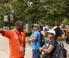 A tour guide wearing an orange shirt gestures while leading a group of tourists on a city street