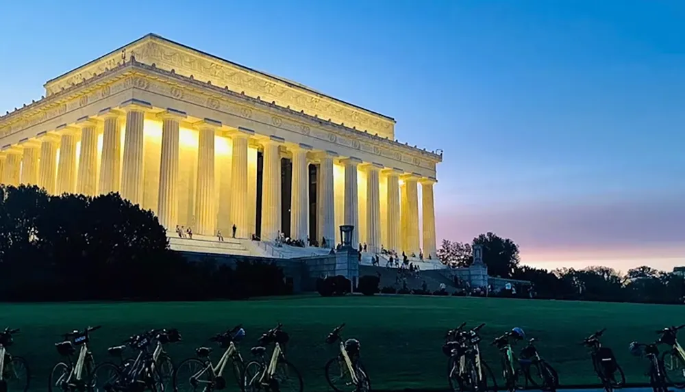 The image shows the Lincoln Memorial illuminated at dusk with several bicycles lined up in the foreground