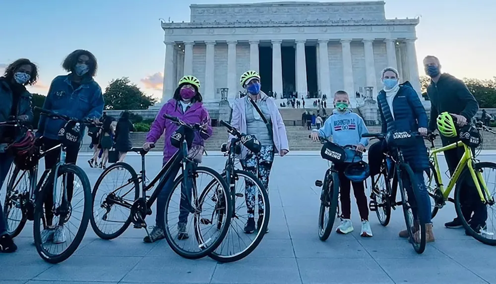 A group of people wearing masks and helmets stand with bicycles in front of the Lincoln Memorial