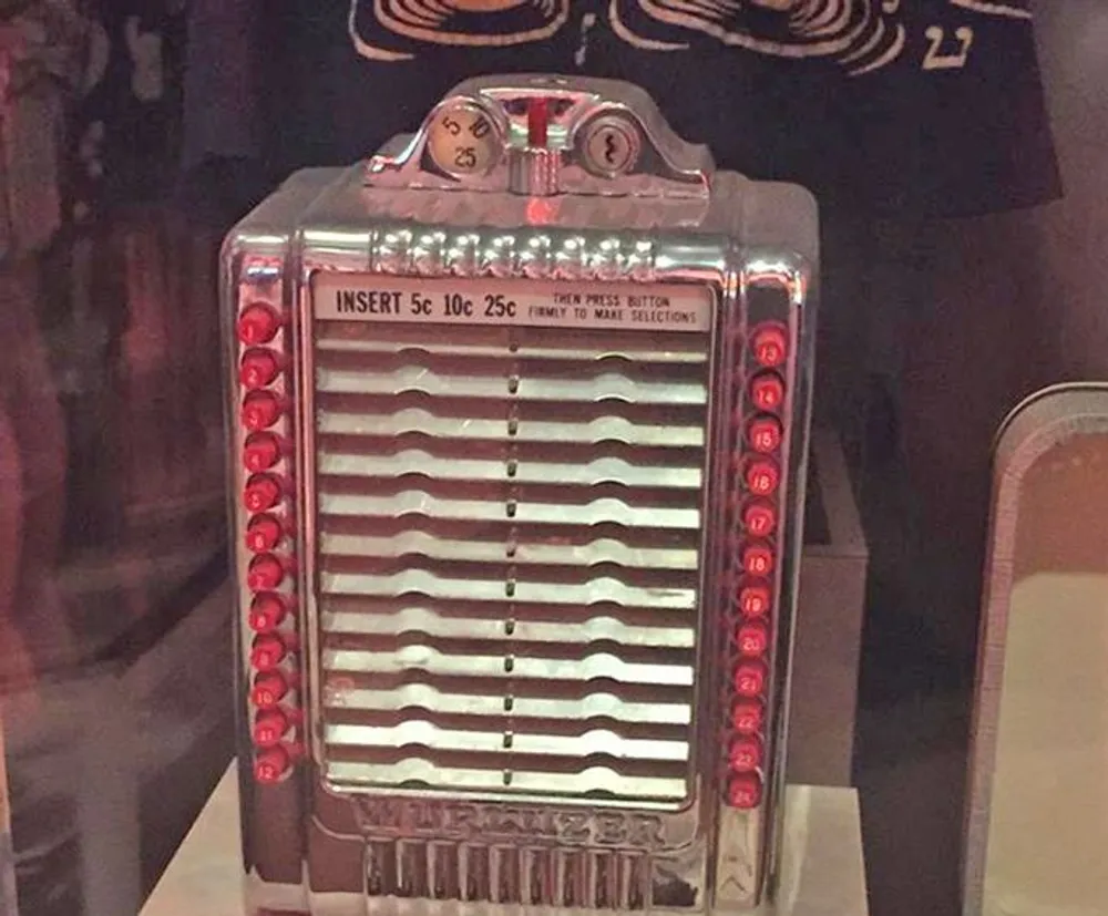 The image shows a vintage coin-operated tabletop jukebox selector with instructions to insert 5 10 or 25 cents before pressing a button to make selections