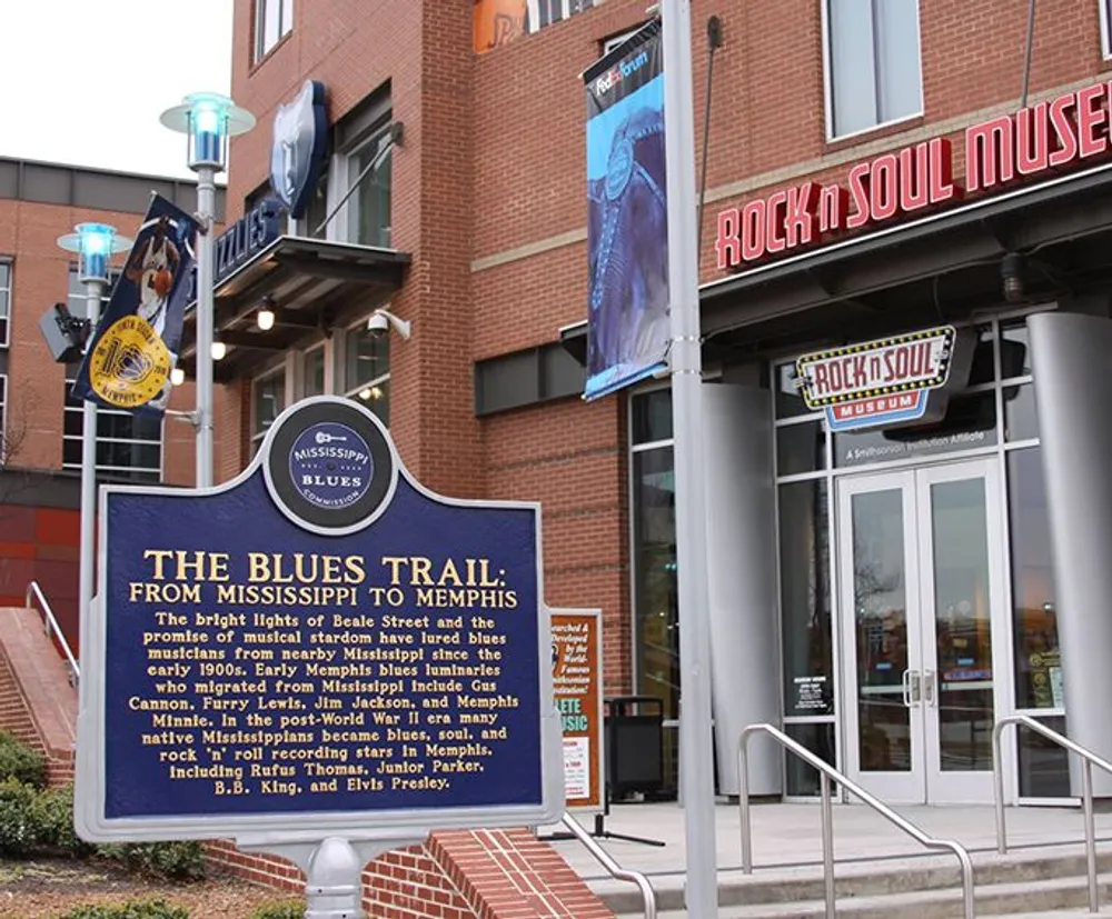 The image captures a historical marker for The Blues Trail From Mississippi to Memphis in front of the Rock n Soul Museum celebrating the musical migration and influential artists of the genre